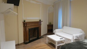Une pièce avec une cheminée, un canapé blanc, une petite table et un téléviseur fixé au mur.