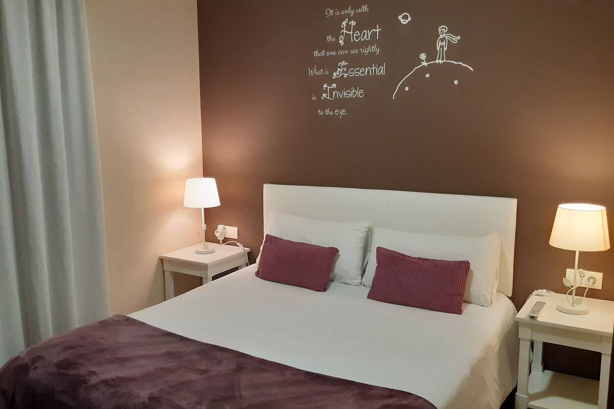 A hotel room with a bed, two bedside tables, and a wall with a motivational quote.