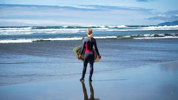 A person in a wetsuit carrying a surfboard on a beach with waves in the background.