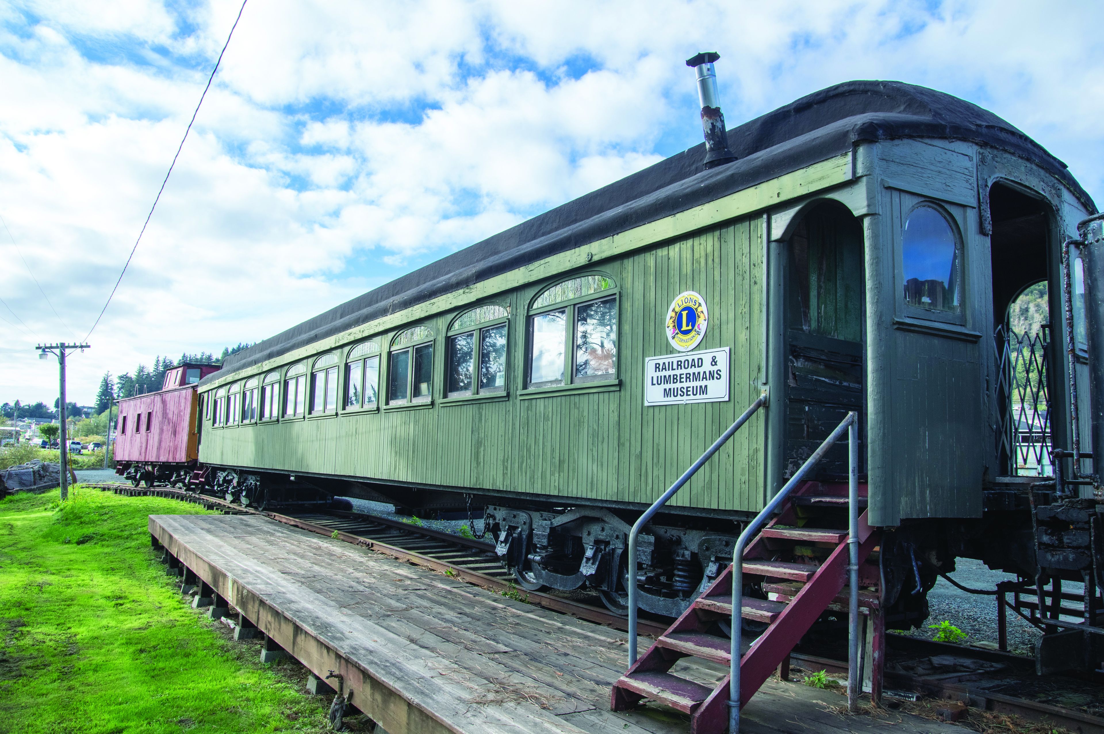 A green vintage train car with a sign reading "Lumbermans Museum" parked on tracks.