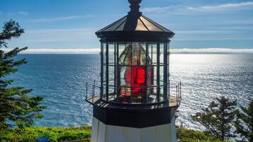 Un faro con cerramiento de vidrio, rodeado de vegetación y con vistas al mar.