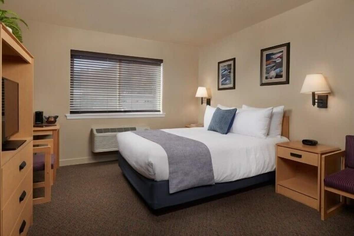 A hotel room with a bed, bedside tables, a desk, a chair, a radiator, and two wall-mounted lamps.