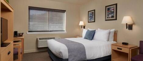 A hotel room with a bed, bedside tables, a desk, a chair, a radiator, and two wall-mounted lamps.