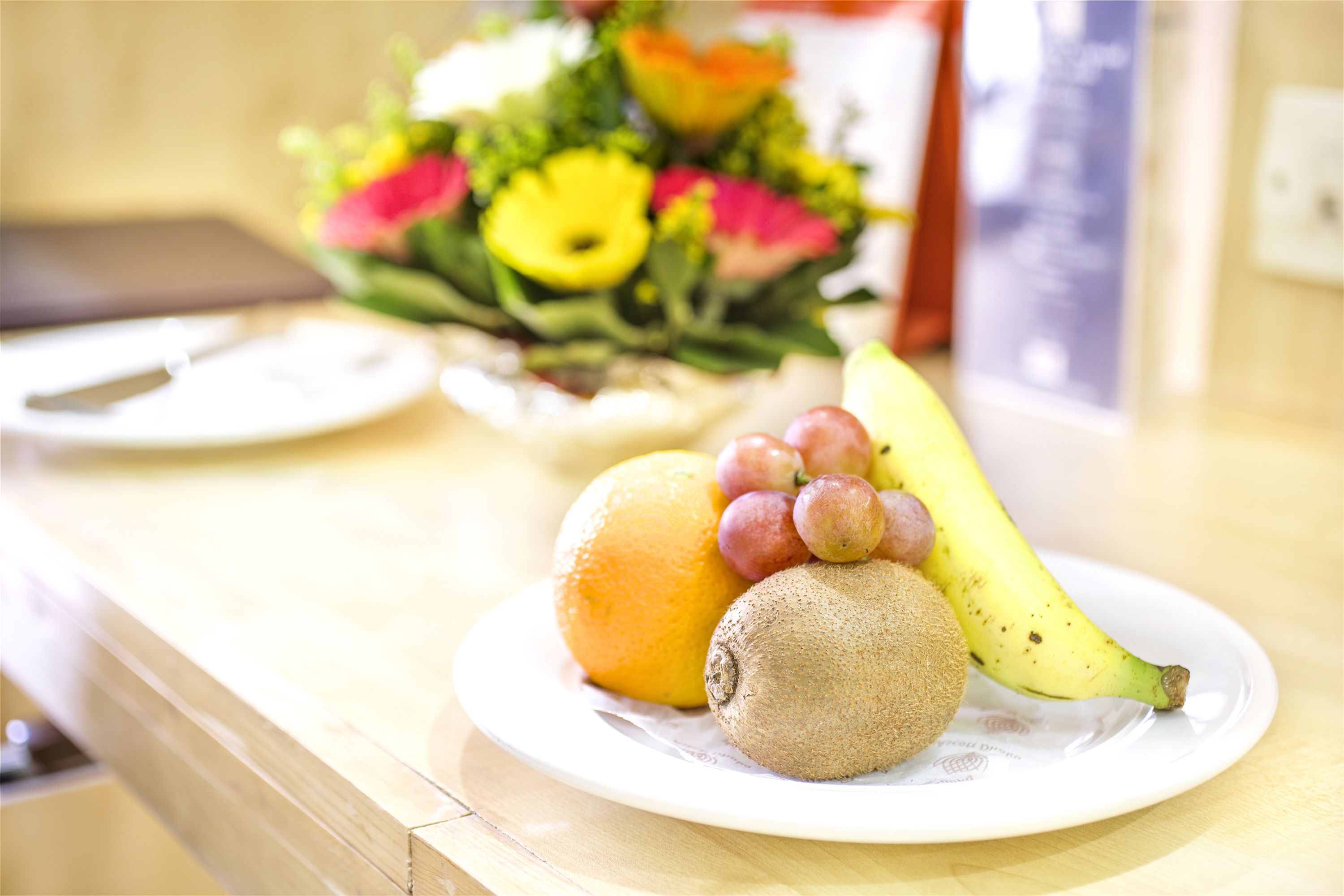 Un plato con un kiwi, una naranja y un plátano sobre una mesa de madera.