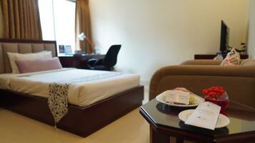 Habitación de hotel con cama, escritorio y silla, sofá, y una mesa con un plato, un vaso de bebida roja y una tarjeta.