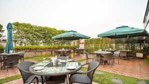 Un'area patio esterna con tavoli e sedie rotondi, ombrelloni verdi e pavimento in mattoni.