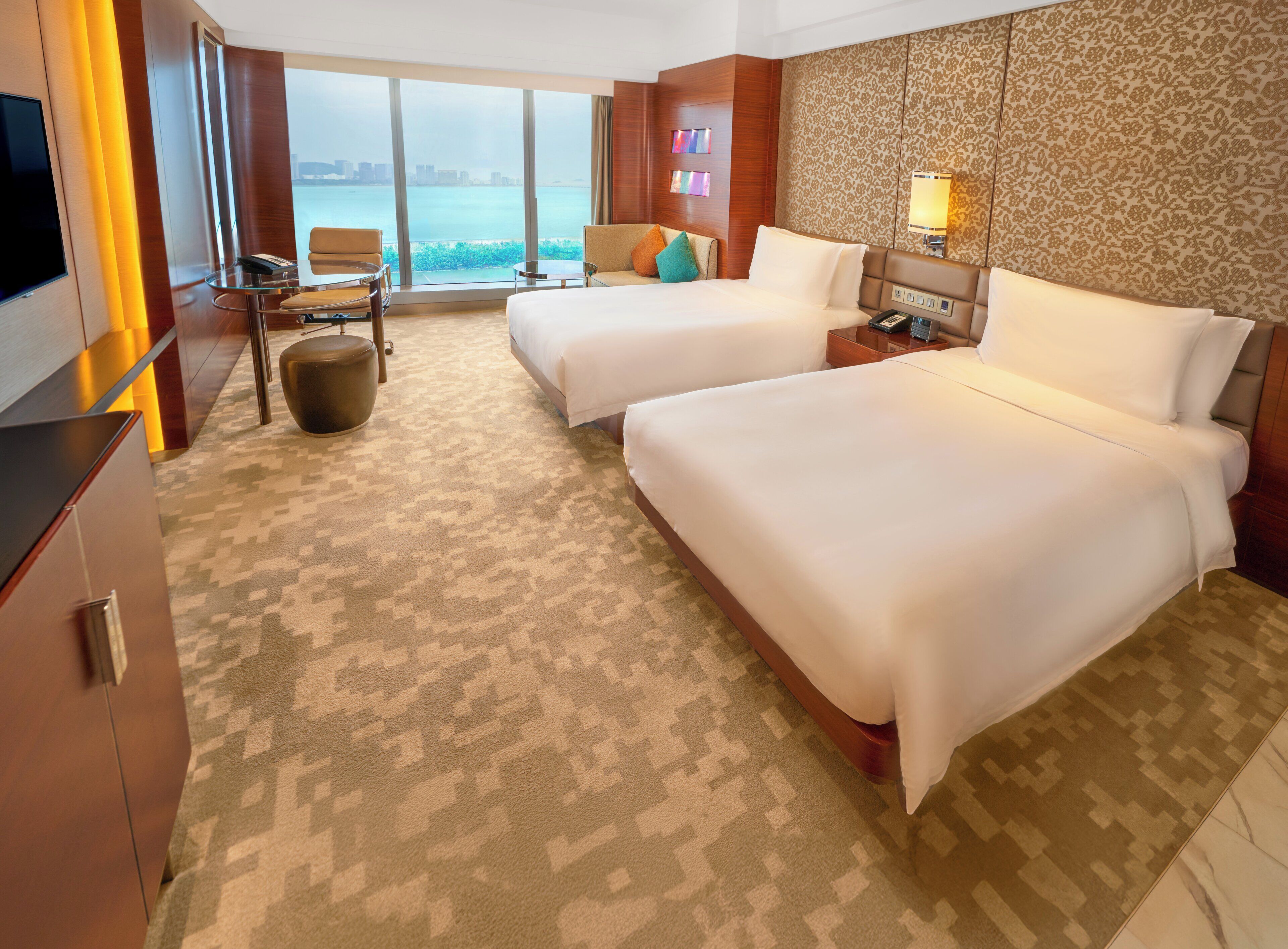 Quarto de hotel com duas camas, televisão, uma mesinha e vista para a cidade.