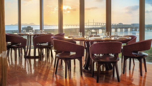 A restaurant with large windows overlooking a body of water and a bridge, featuring wooden flooring and upholstered chairs. - Crowne Plaza Macau by IHG (Macau)