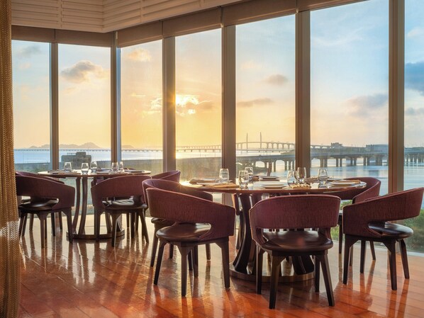 A restaurant with large windows overlooking a body of water and a bridge, featuring wooden flooring and upholstered chairs. - Crowne Plaza Macau by IHG (Macau)