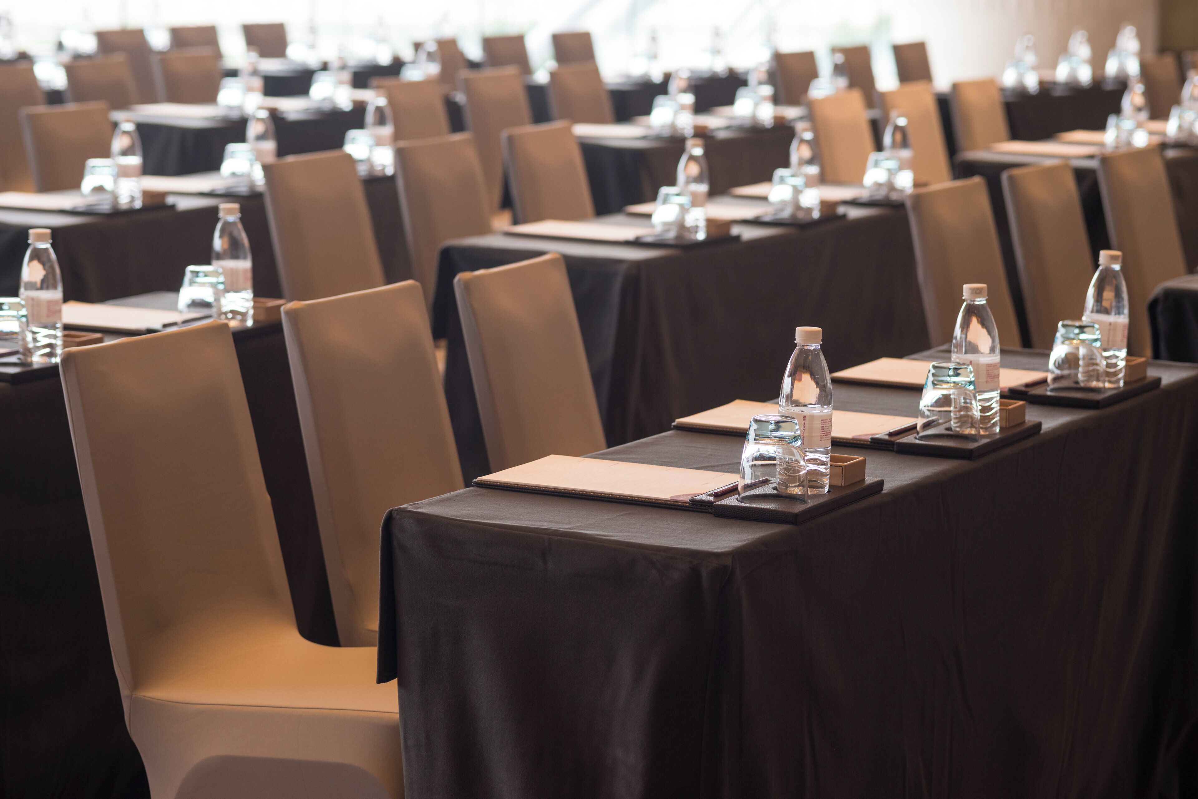 A conference room with rows of tables, chairs, water bottles, and notepads.