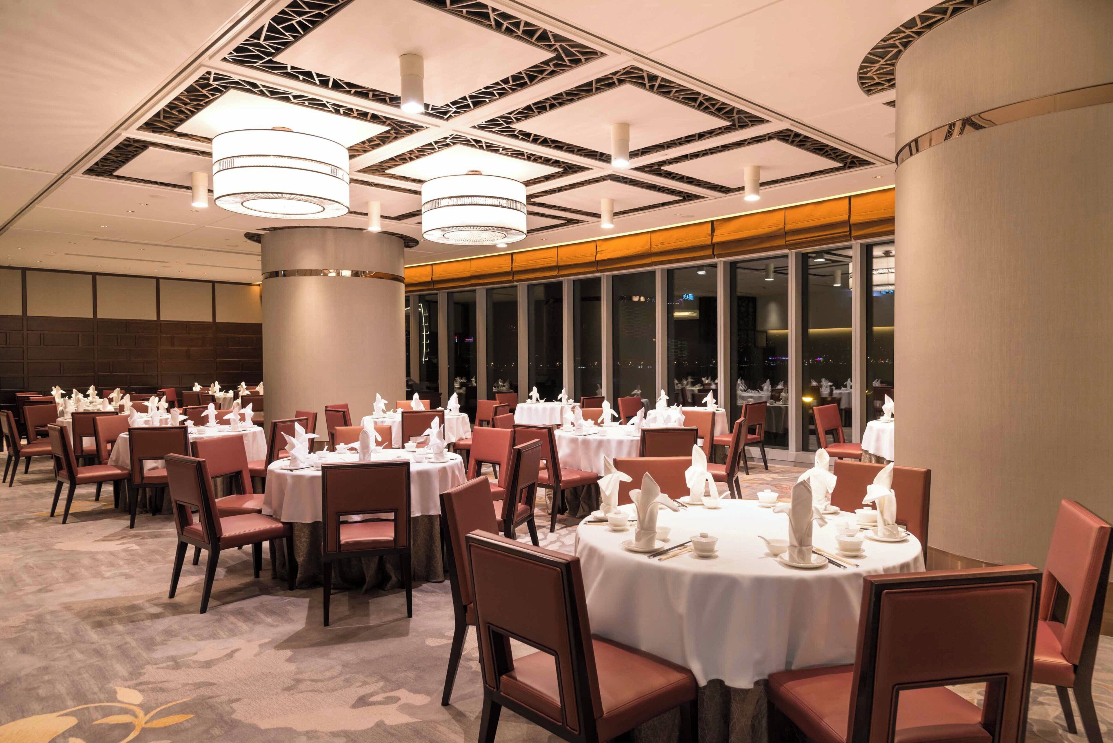 A hotel dining area with round tables, chairs, and a modern ceiling design.