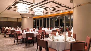 A hotel dining area with round tables, chairs, and a modern ceiling design.