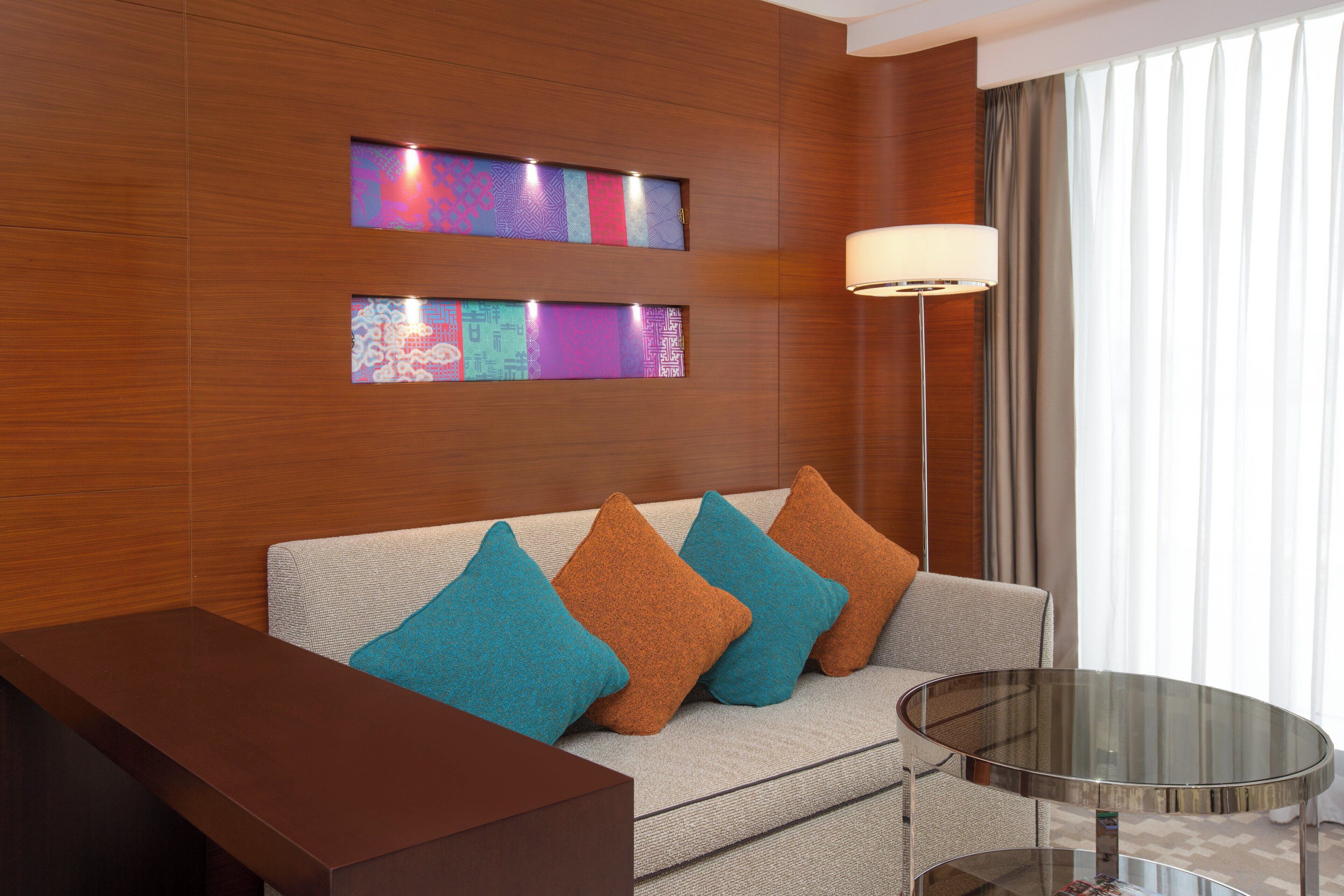 A modern hotel room with a sofa, a glass coffee table, and a lamp.