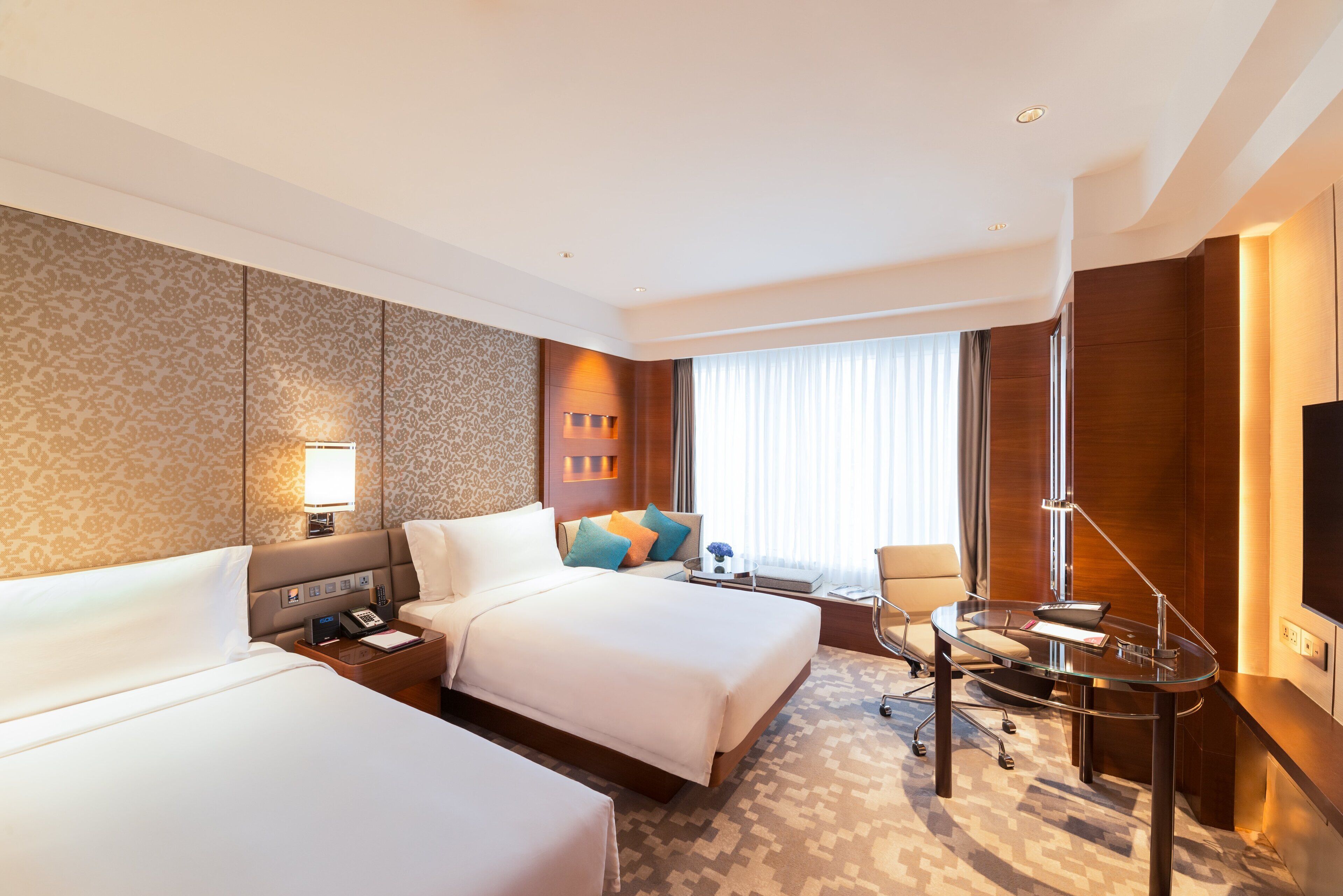 A hotel room with two beds, a desk, a chair, a TV, and a window with curtains.