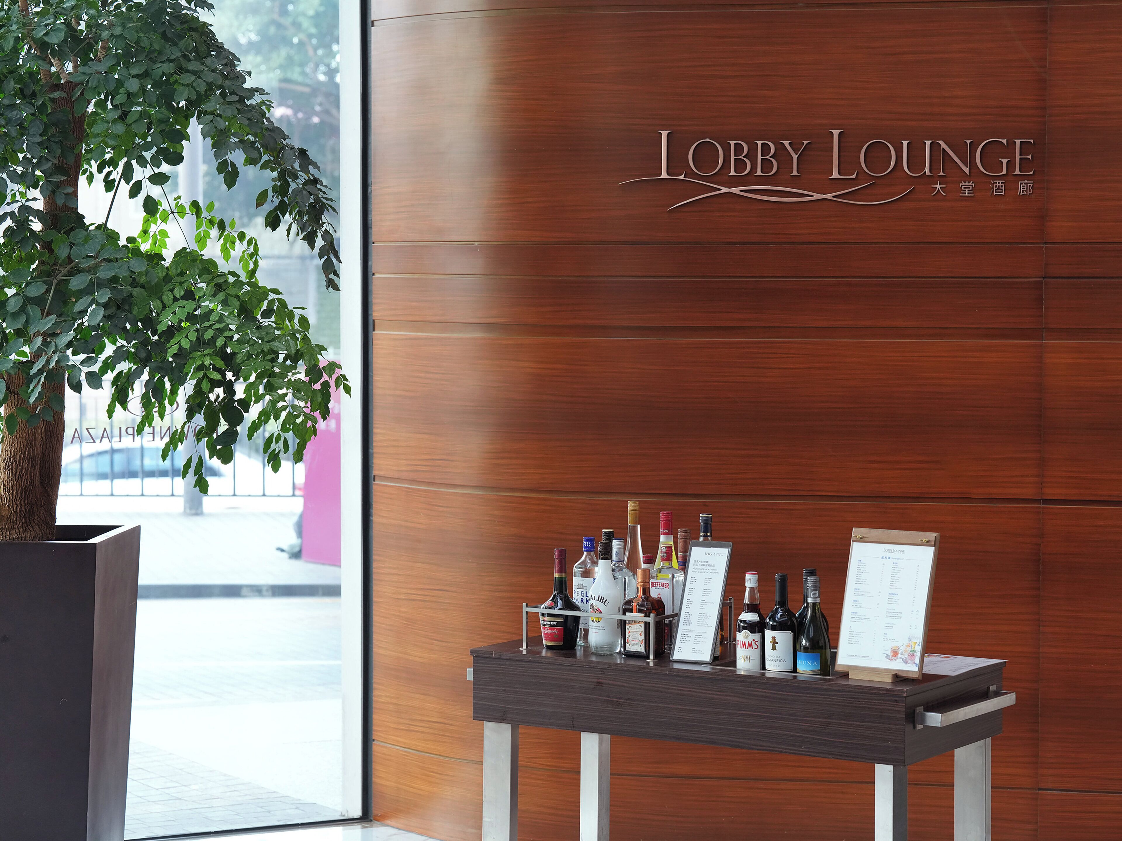 A lobby lounge with a wooden wall and a sign reading "Lobby Lounge". There is a table with various bottles and a menu stand.