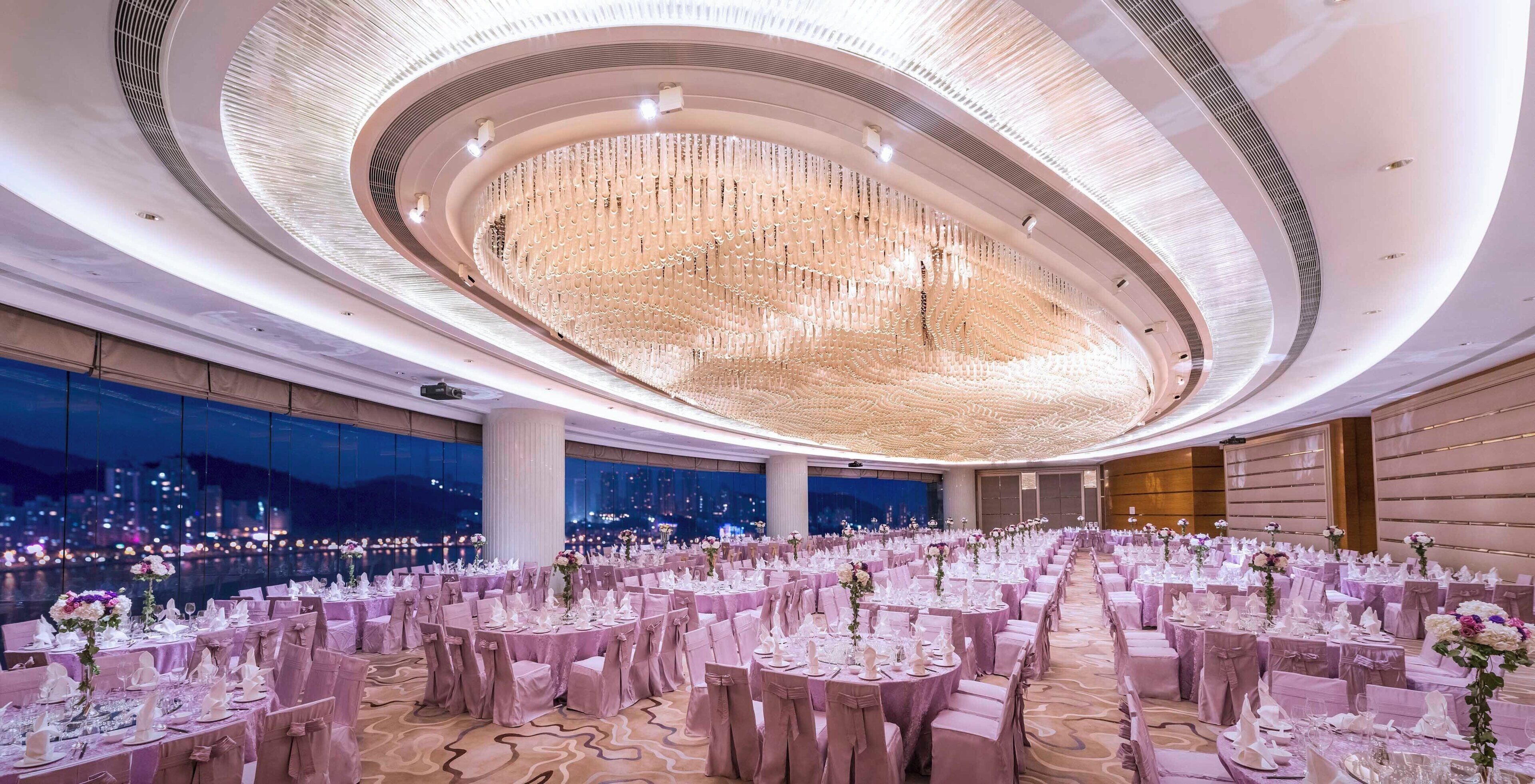 Un amplio salón de banquetes con mesas redondas, elegantes candelabros y vistas a la ciudad.