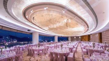 Un amplio salón de banquetes con mesas redondas, elegantes candelabros y vistas a la ciudad.