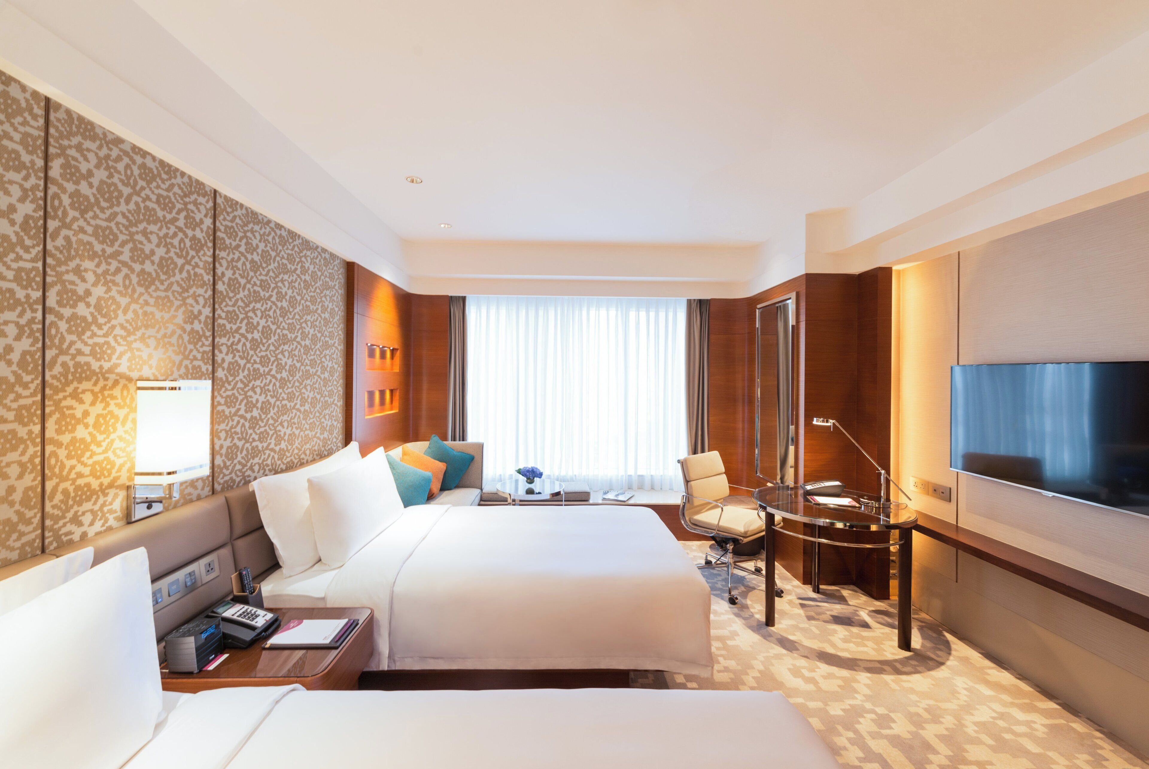 Une chambre d’hôtel avec un grand lit, un bureau avec un téléphone, une chaise, une télévision et une fenêtre avec des rideaux.
