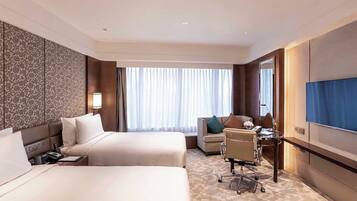 A hotel room with two beds, a desk, a chair, a TV, and a large window with curtains.