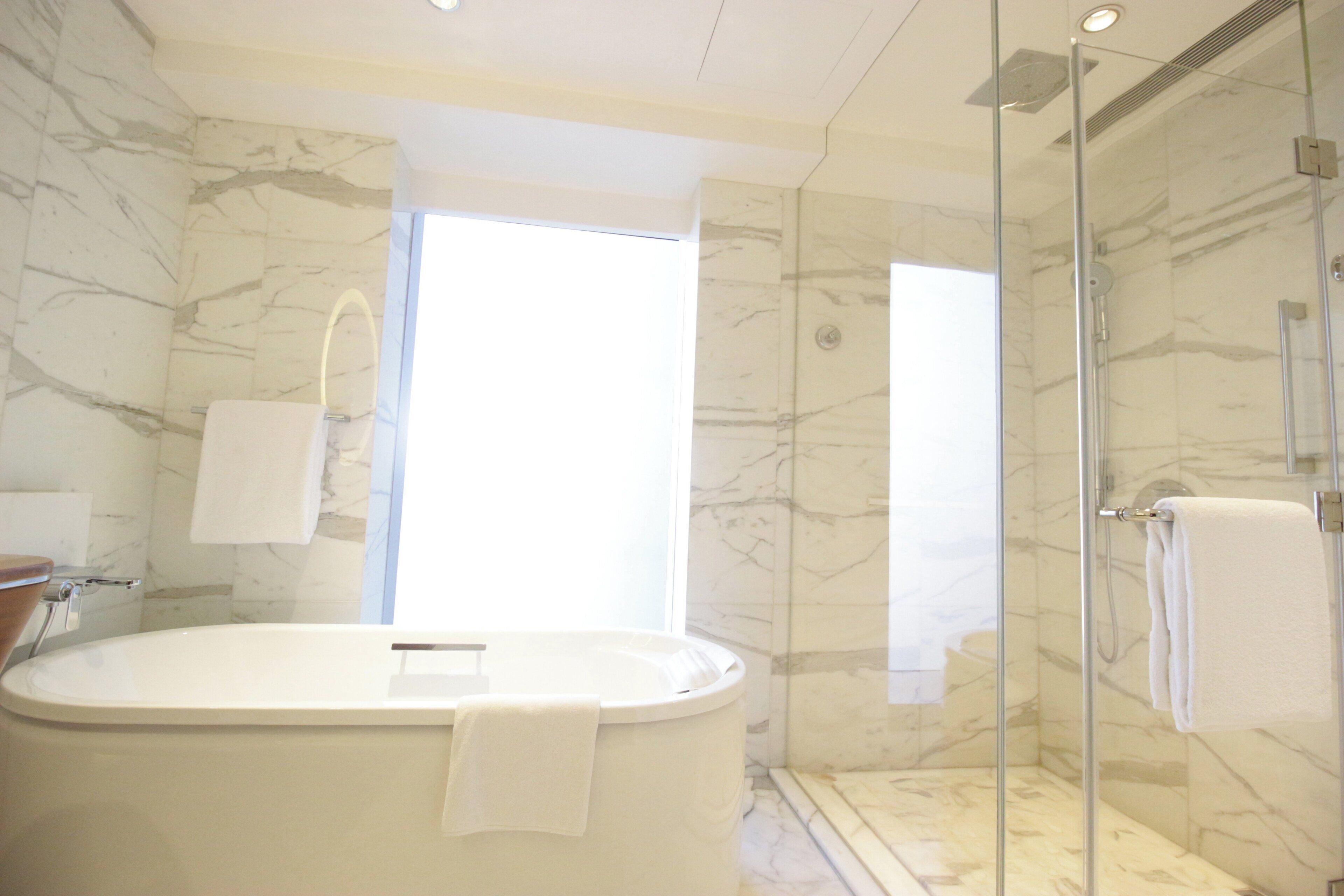 A bathroom with a marble wall, a glass-enclosed shower, and a white bathtub.
