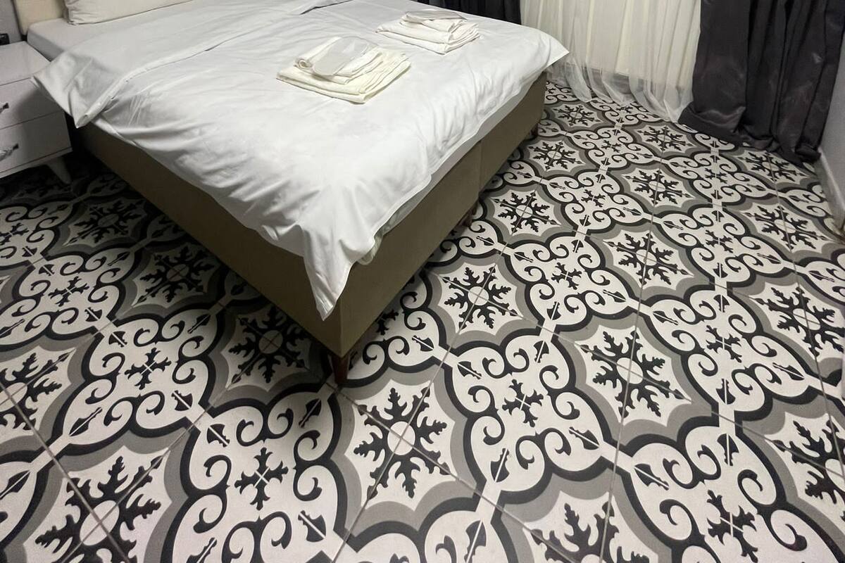 Un lit bien fait, avec du linge de lit blanc, une table de chevet avec une lampe et un sol à motifs.