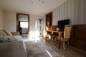 A living room with a sofa, a dining table with chairs, a television, and a coat stand. - Suite Dreams Istanbul (Istanbul)