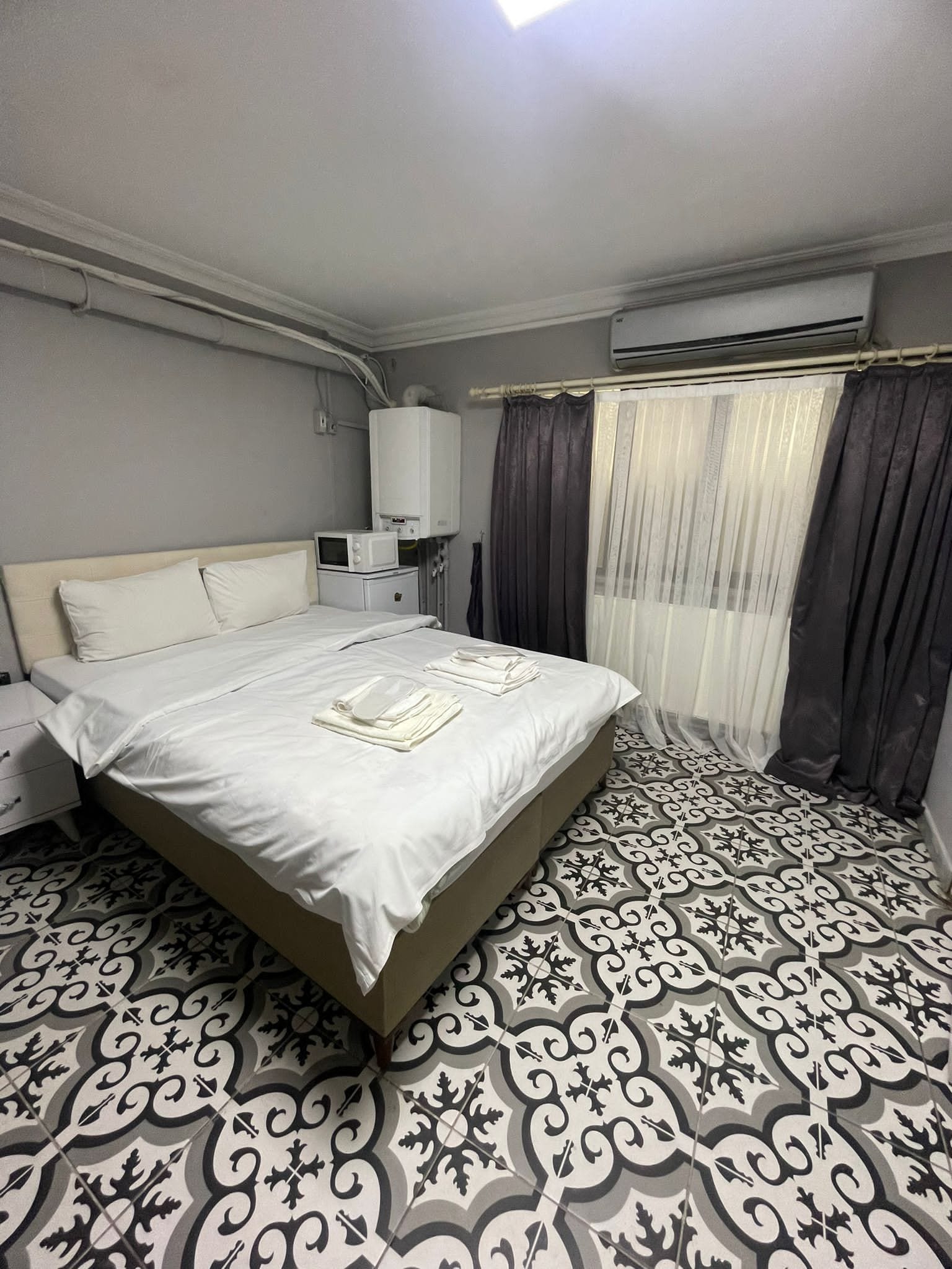 Un lit bien fait, avec du linge de lit blanc, une table de chevet avec une lampe et un sol à motifs.