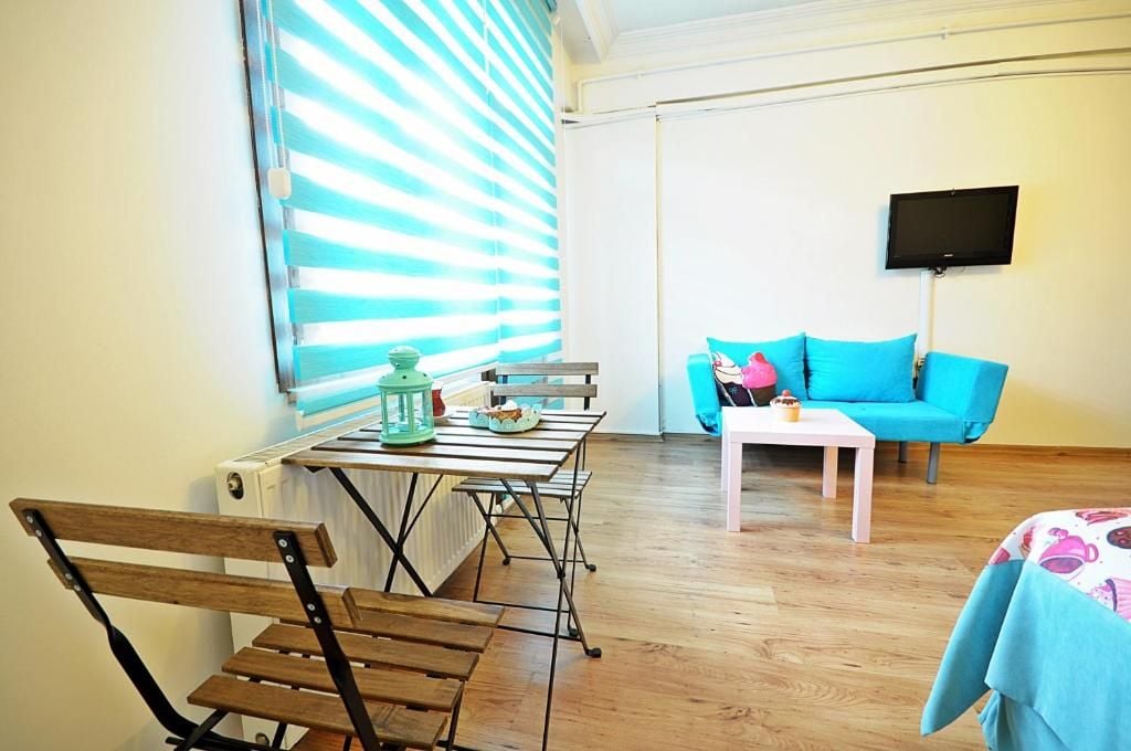 A room with a wooden table, chairs, a blue sofa, a white coffee table, and a television mounted on the wall.