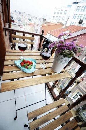 A balcony with a wooden table, a potted plant, a glass of red wine, and a plate of strawberries. - Suite Dreams Istanbul (Istanbul)