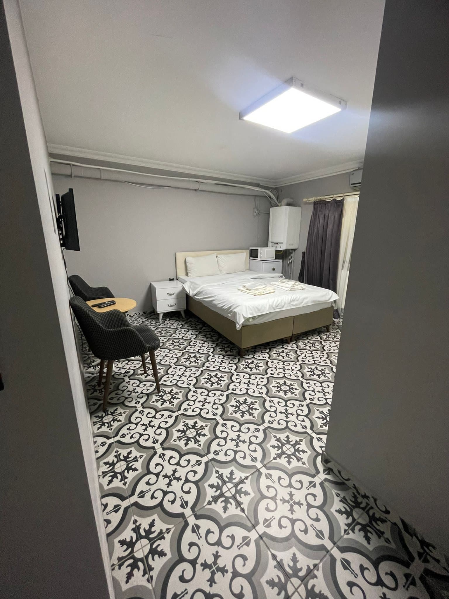 A bedroom with a bed, bedside tables, a chair, a flat-screen TV, and patterned flooring.