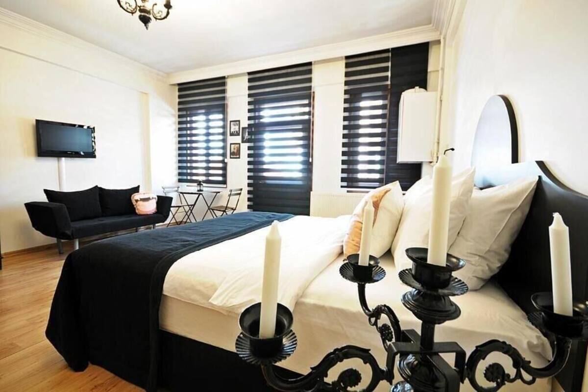 Une chambre à coucher avec un lit, une literie noire et blanche, un téléviseur, un canapé noir et un lustre.