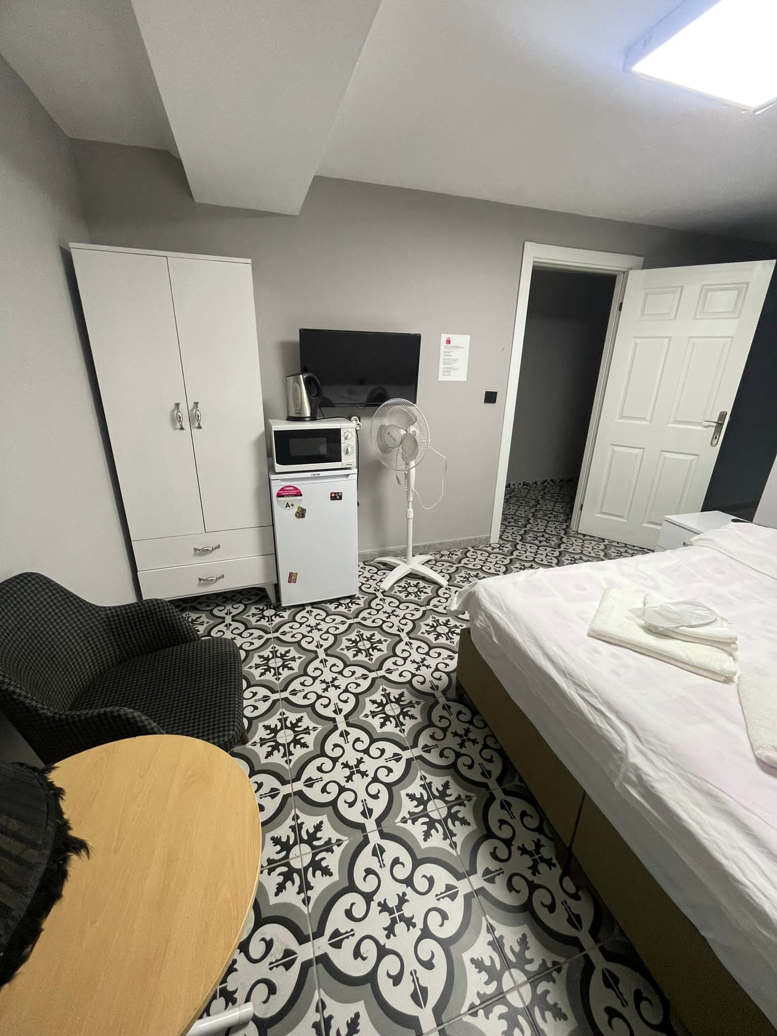 A hotel room with a bed, a desk, a wardrobe, a television, and a fan.