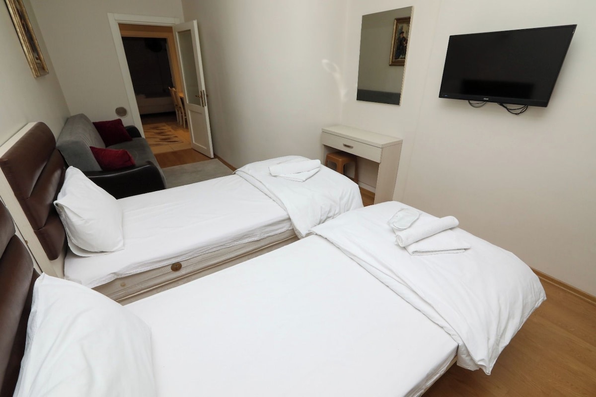 A hotel room with two beds, a desk, a chair, a TV, and a mirror.