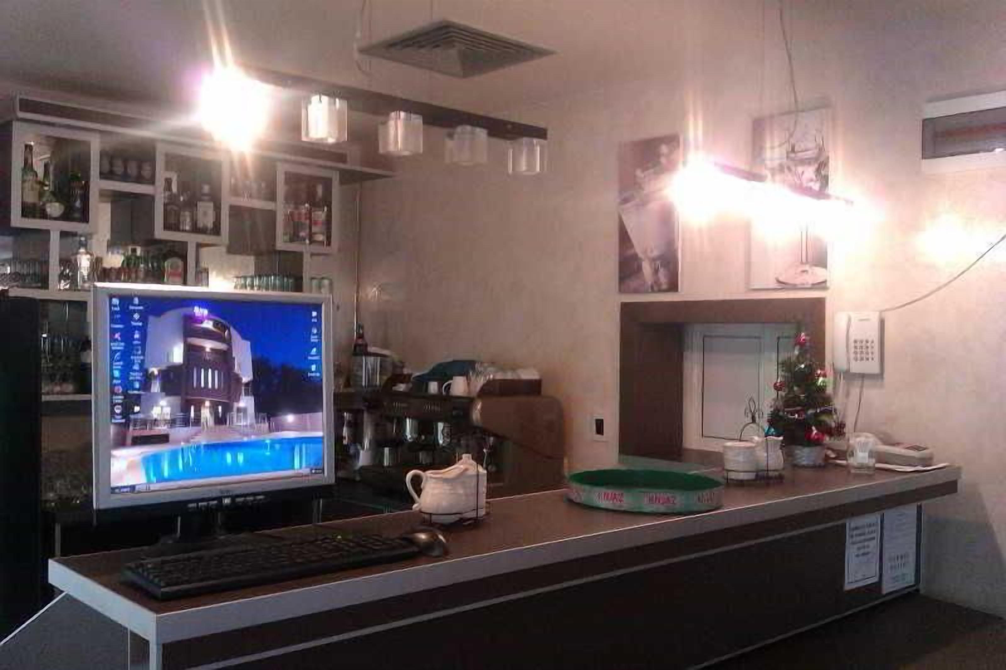 A reception desk with a computer monitor, keyboard, and mouse. There is a bar area with shelves of bottles and a small Christmas tree.