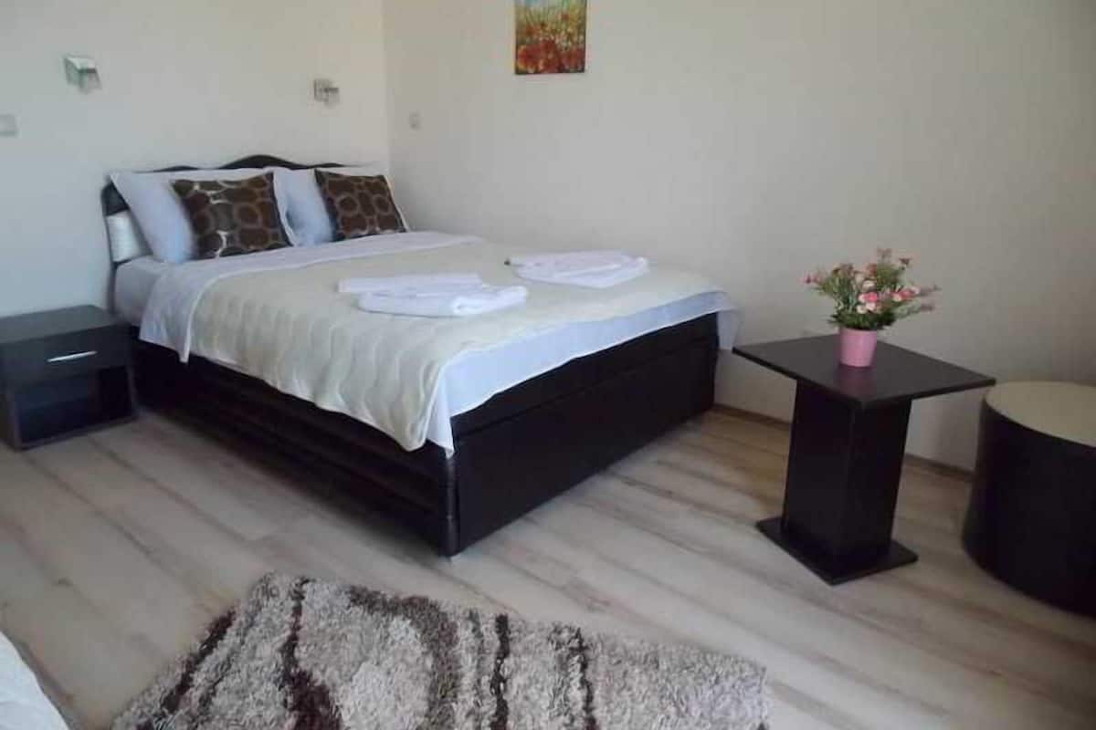 A neatly arranged bedroom with a bed, bedside tables, a small table with a plant, and a painting on the wall.
