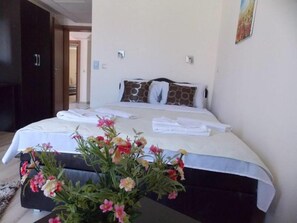 A hotel room with a bed, pillows, a vase of flowers, and a neatly made bed with towels. - Villa Dnd Niska Banja (Niš)