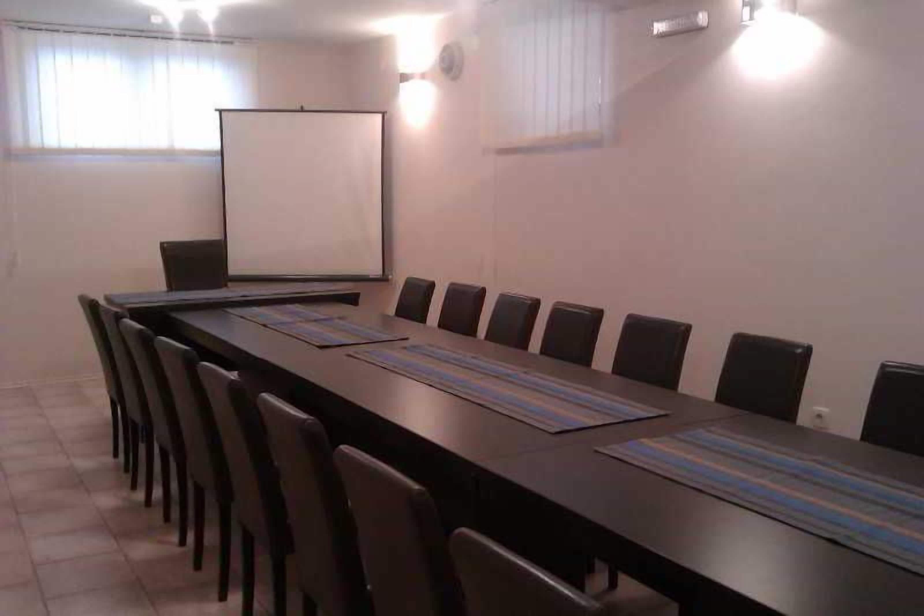 A conference room with a long table, chairs, a projector screen, and a whiteboard.