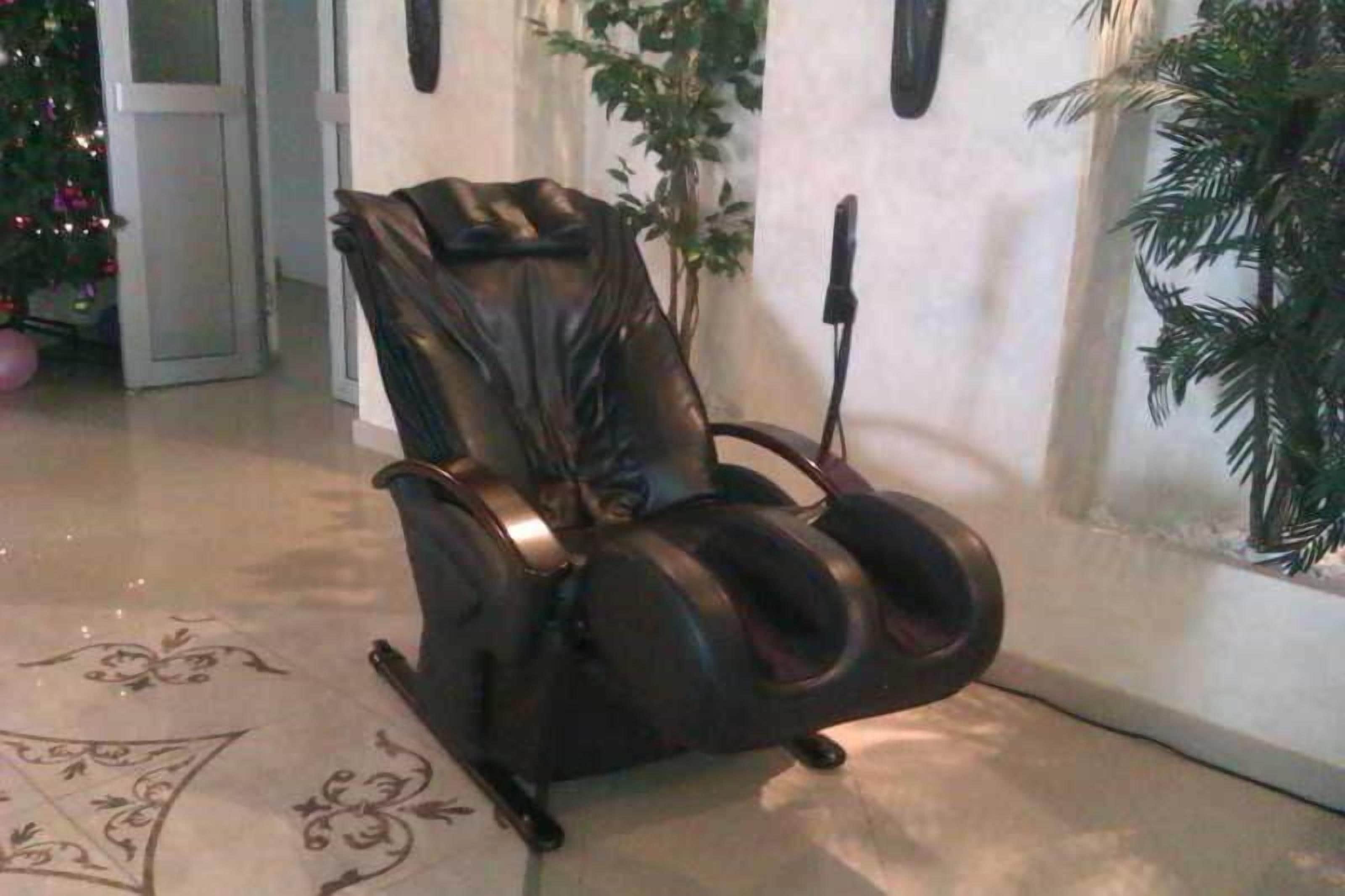A massage chair in a room with a tiled floor, a potted plant, and a wall-mounted light fixture.