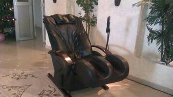 A massage chair in a room with a tiled floor, a potted plant, and a wall-mounted light fixture.