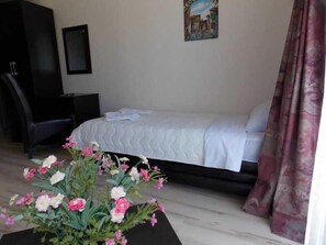A bedroom with a bed, a nightstand, a desk, a chair, and a vase with flowers. - Villa Dnd Niska Banja (Niš)