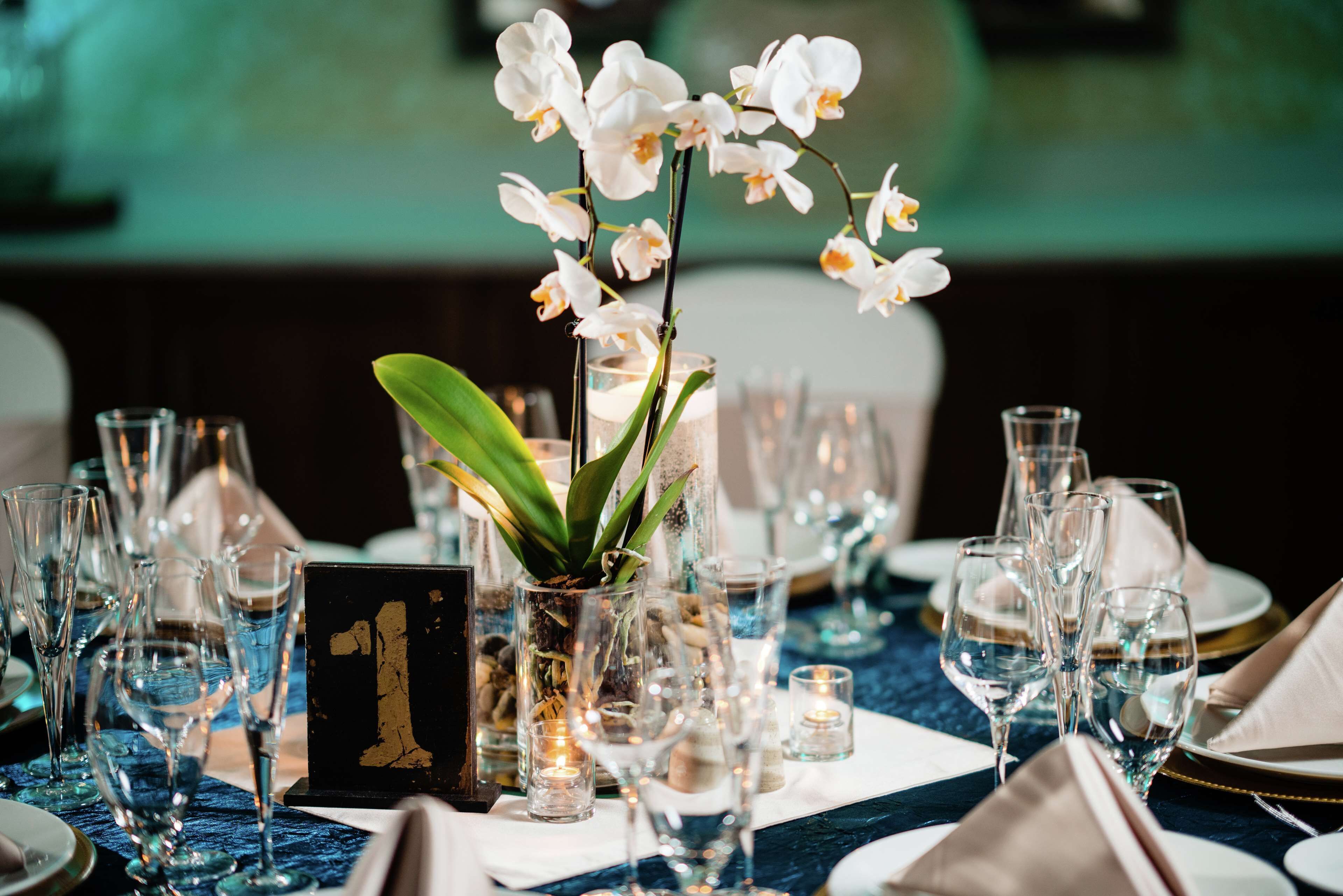 A table set for a formal event with clear glassware, a centerpiece with white orchids, and a numbered sign.