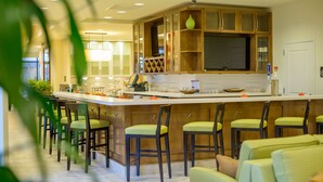A modern kitchen with a bar area, wooden cabinets, and green chairs. - Hilton Garden Inn Exton / West Chester (Exton)