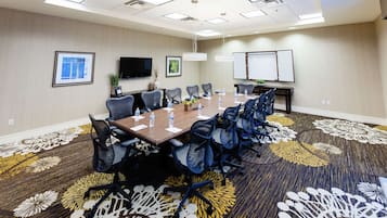 Uma sala de conferências com uma mesa comprida, cadeiras, uma TV e um quadro branco.