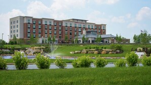 A multi-story hotel with a brick facade, a landscaped garden with a pond and fountain, and a clear sky. - Hilton Garden Inn Exton / West Chester (Exton)
