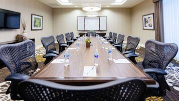 A conference room with a long wooden table, black mesh chairs, water bottles, and a projector screen.