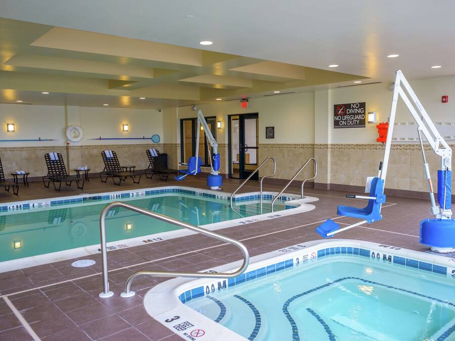 Una piscina cubierta con varias pistas, sillones de descanso y un cartel de prohibición de saltos.