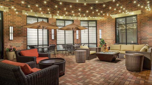 An outdoor patio with wicker furniture, brick flooring, and string lights. - Hilton Garden Inn Exton / West Chester (Exton)