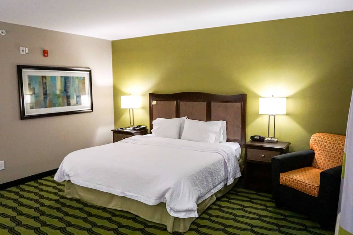 Una camera d'albergo con un letto grande, due comodini con lampade, una sedia, un quadro appeso al muro e un tappeto decorato.
