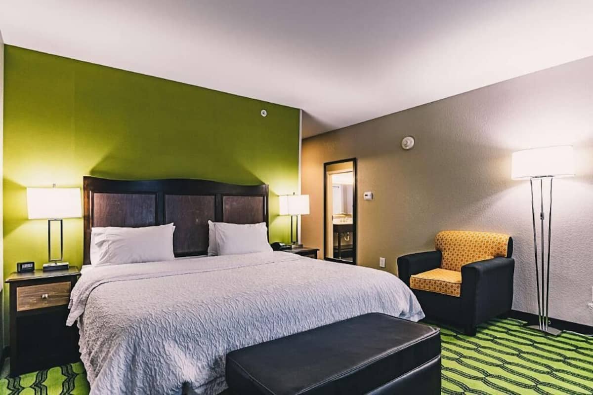 Una camera d'albergo con un letto, una sedia, un comodino, una lampada e una lampada da terra.
