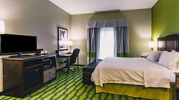 Ein Hotelzimmer mit einem Bett, einem Schreibtisch mit Computer, einem Fernseher und einem grün gemusterten Teppich.
